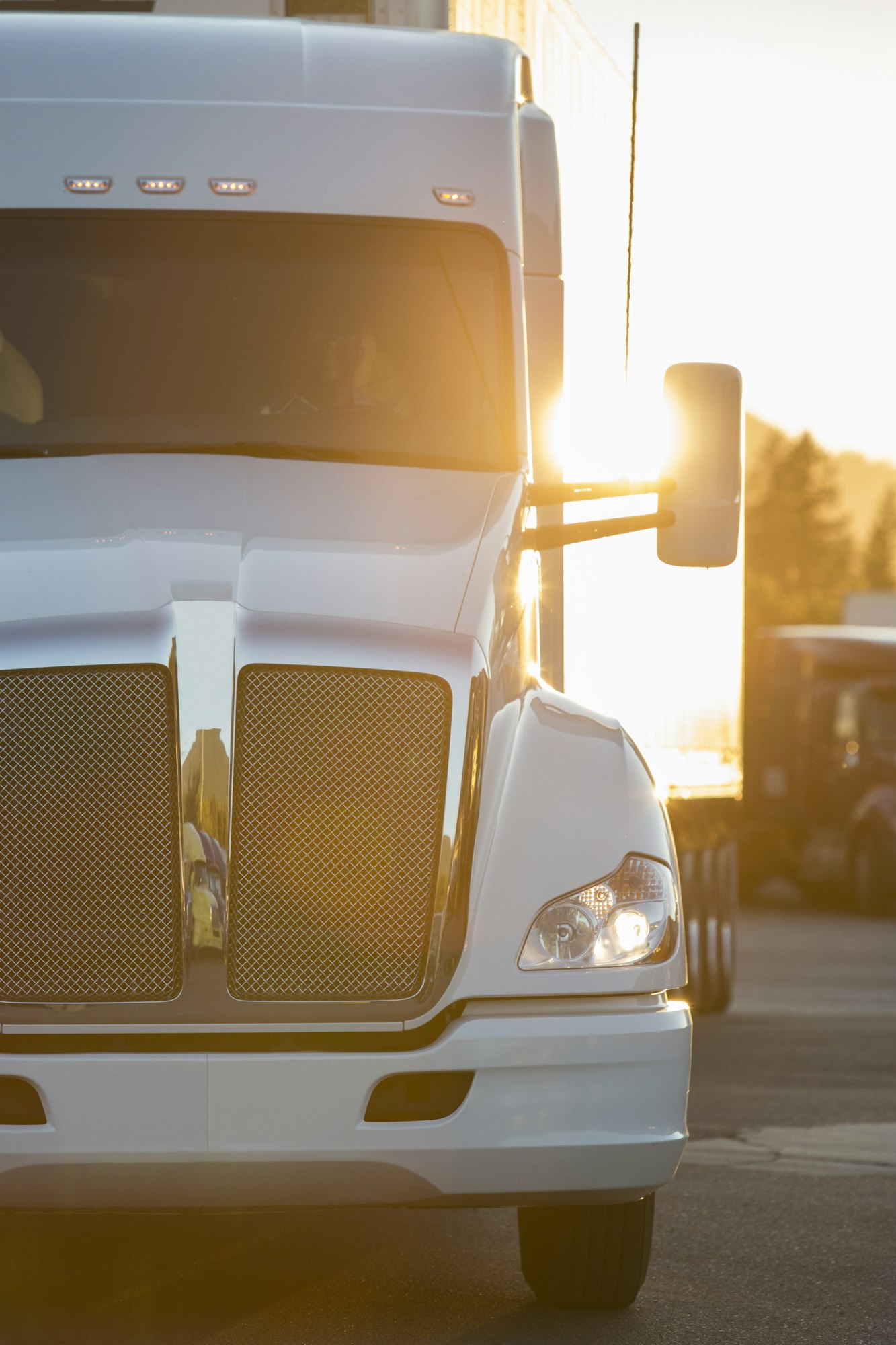 A large commercial truck moving through a truck stop parking lot at sunset.